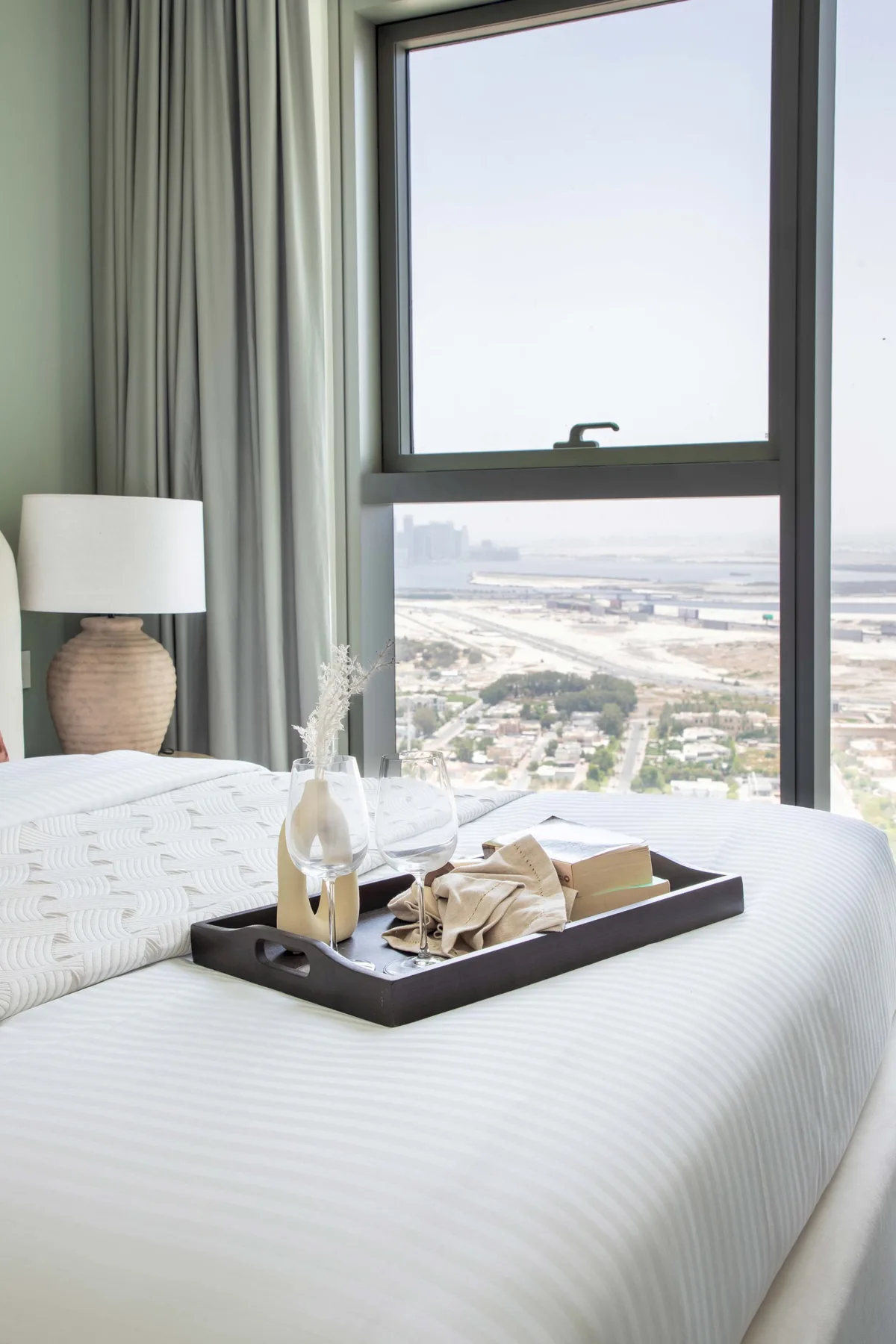Un dormitorio con una cama bien tendida junto a una gran ventana con vistas a la ciudad.