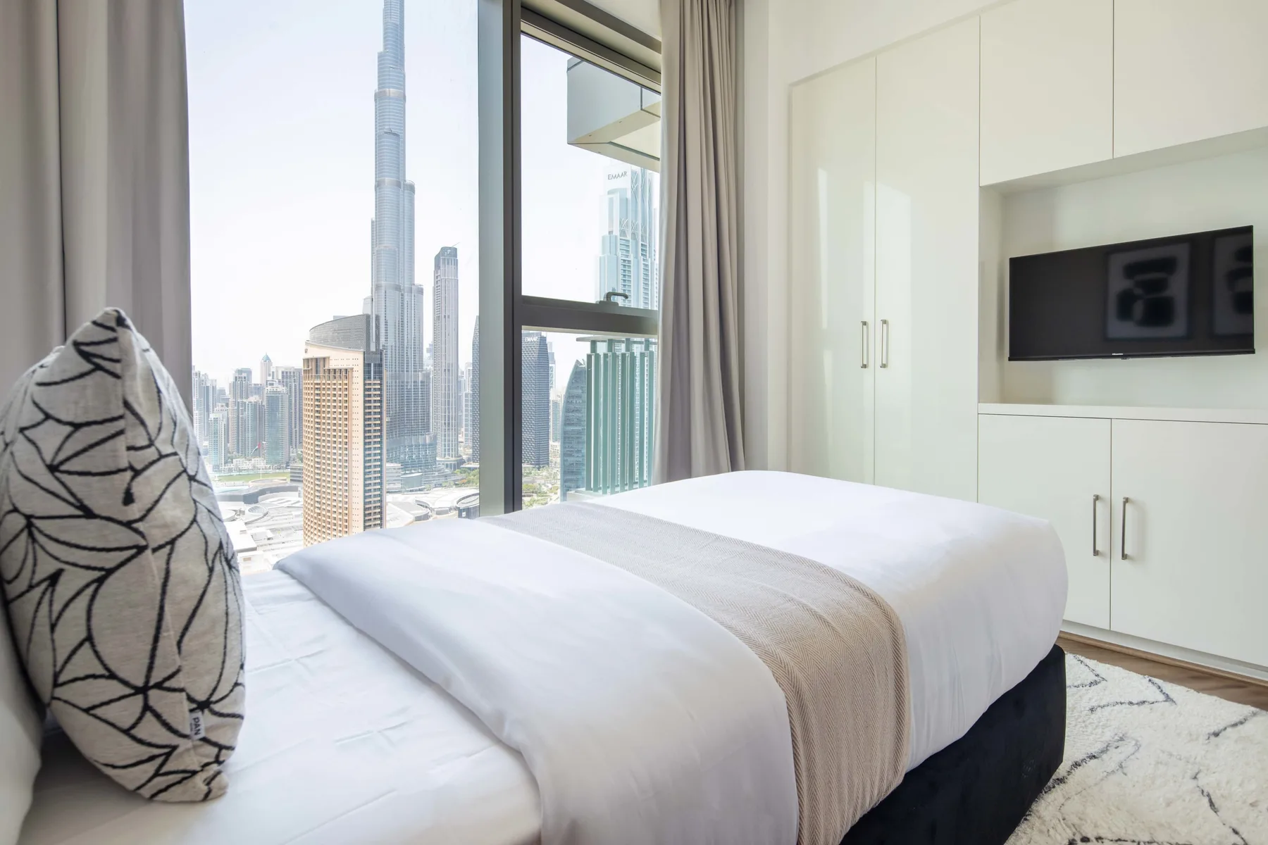 Un dormitorio con una cama tendida junto a una gran ventana con vistas a la ciudad.