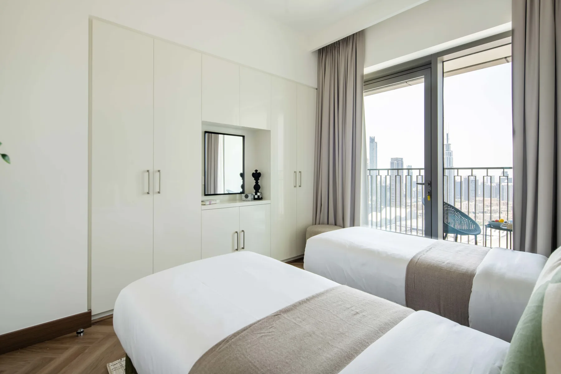 Un dormitorio luminoso con dos camas junto a grandes ventanales con vistas a la ciudad.