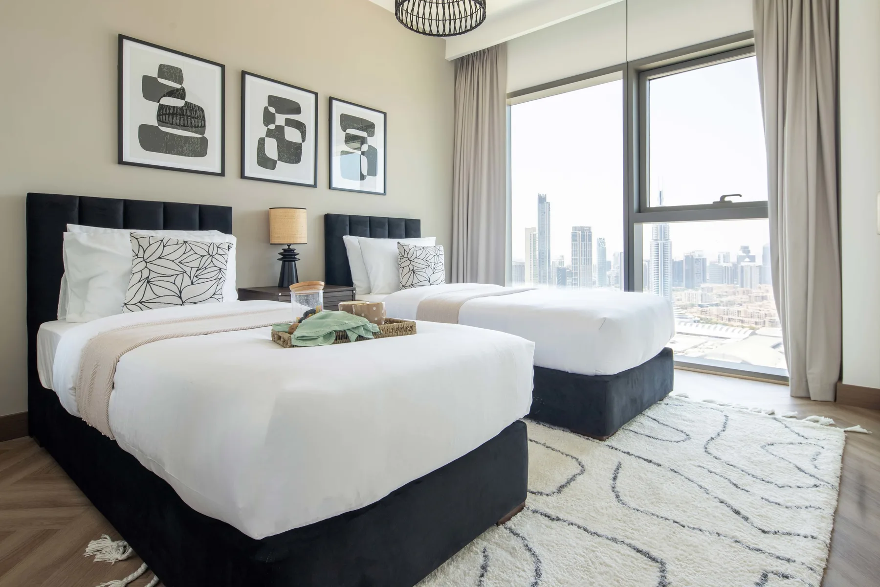 Un dormitorio luminoso con dos camas junto a grandes ventanas con vistas a la ciudad.