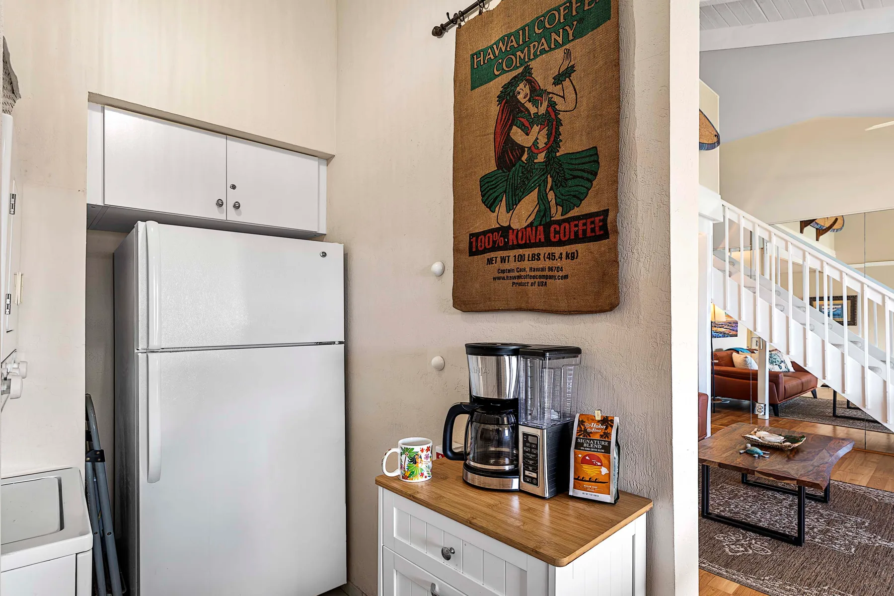 Una cocina con refrigerador y cafetera junto a una sala de estar.