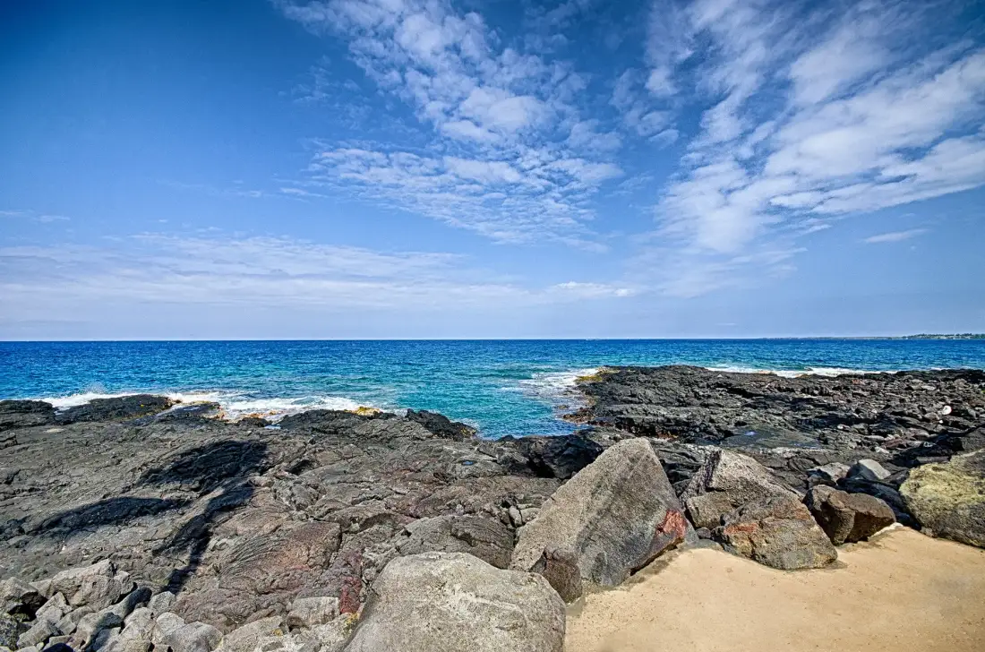 Costa rocosa junto al mar azul bajo un cielo parcialmente nublado.