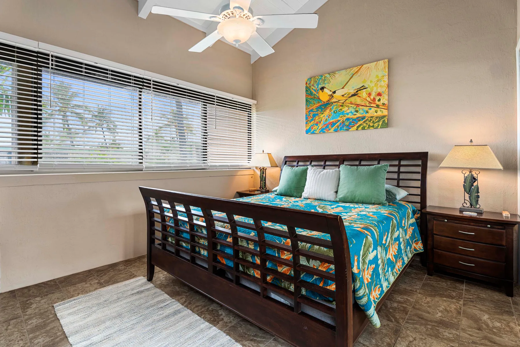 Un dormitorio con una cama de madera oscura, ropa de cama colorida y ventanas amplias.