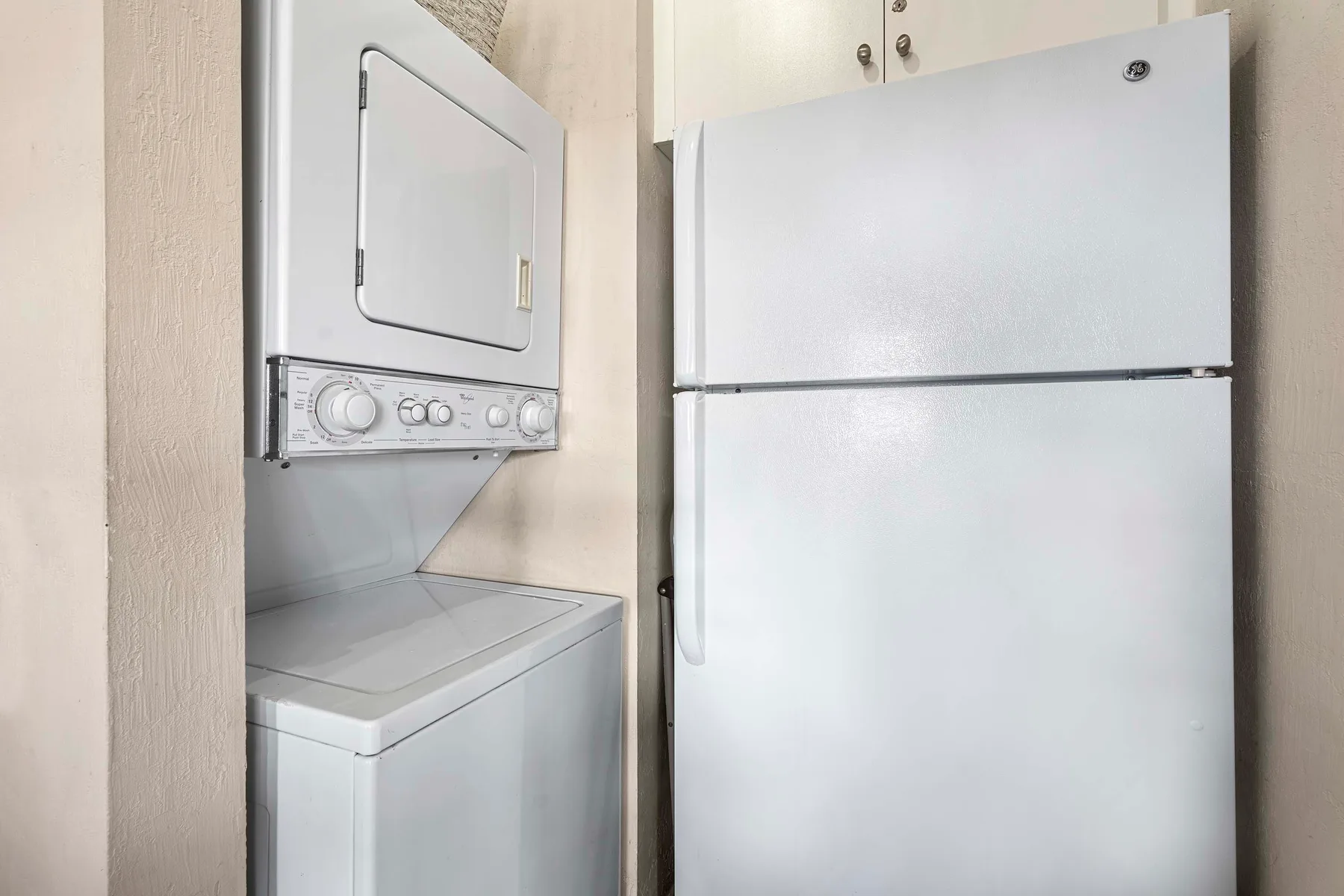 Área de lavandería con una lavadora y secadora apiladas junto a un refrigerador.