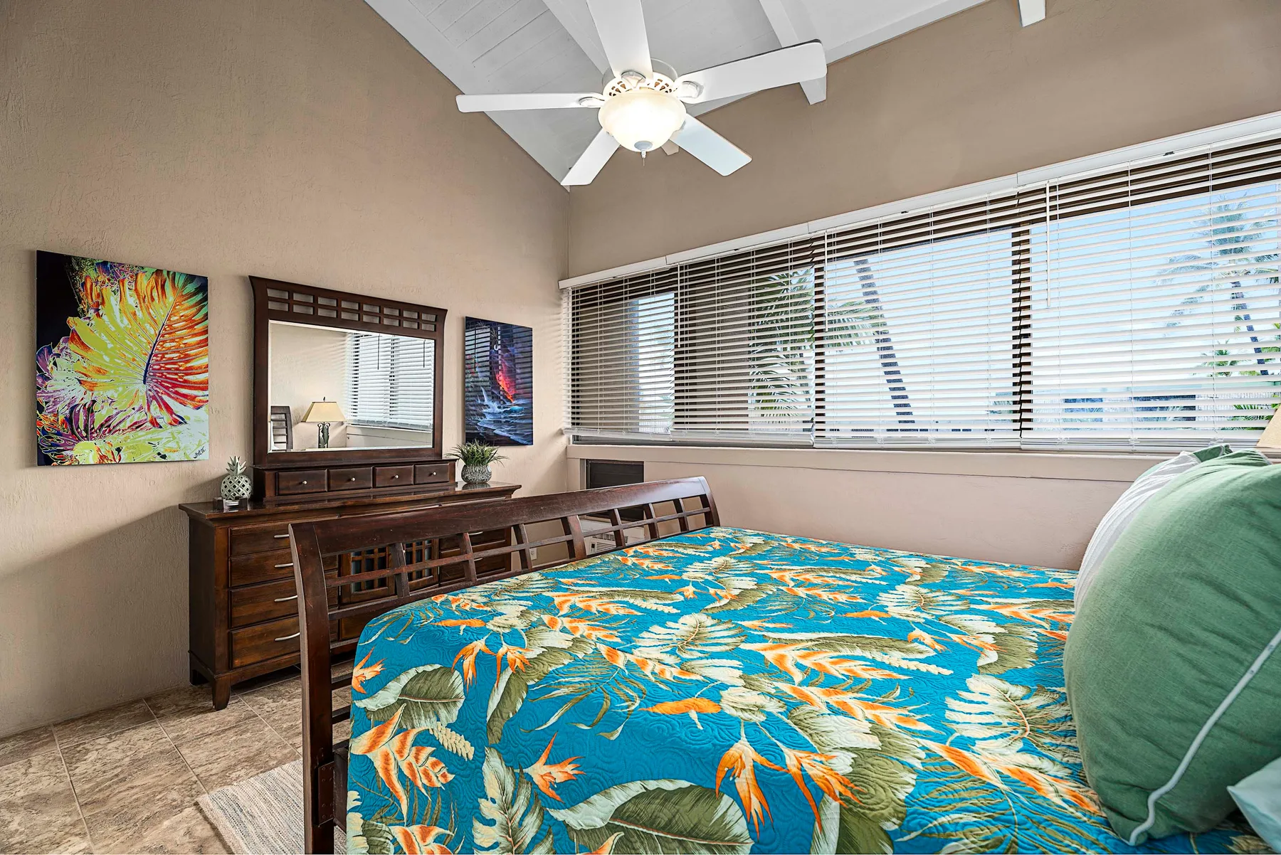 Un dormitorio con una colcha floral colorida y una cómoda de madera bajo la ventana.