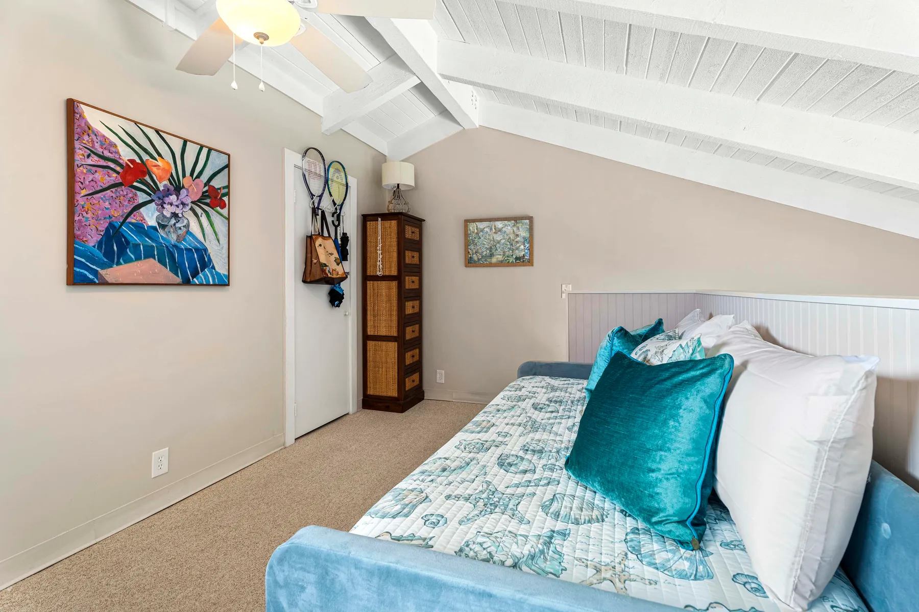 Un dormitorio con una cama vestida de blanco y turquesa bajo un techo inclinado.