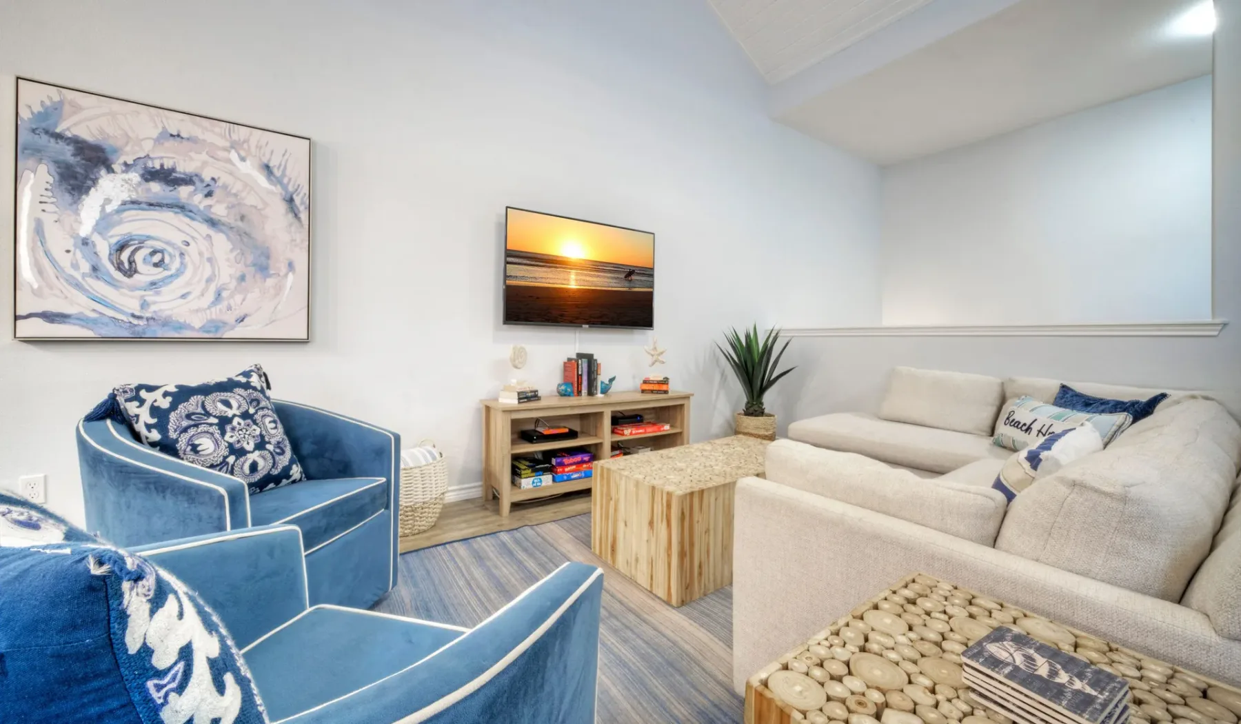 Una sala de estar con asientos azules, un sofá claro y una mesa de centro de madera.