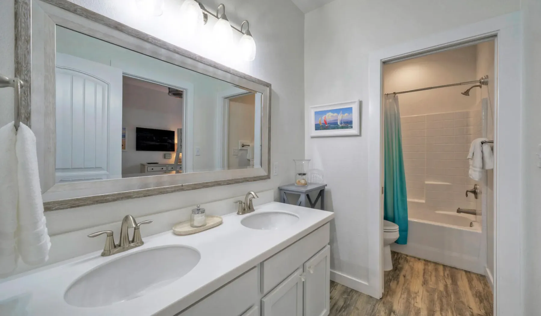 Un tocador de baño con un espejo amplio queda frente a una bañera con ducha.