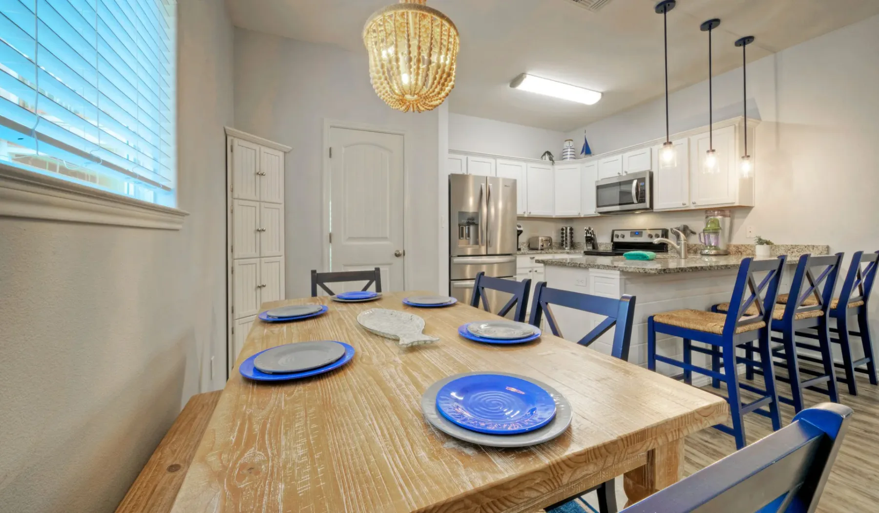 Una mesa de comedor con vajilla azul está junto a una cocina luminosa.