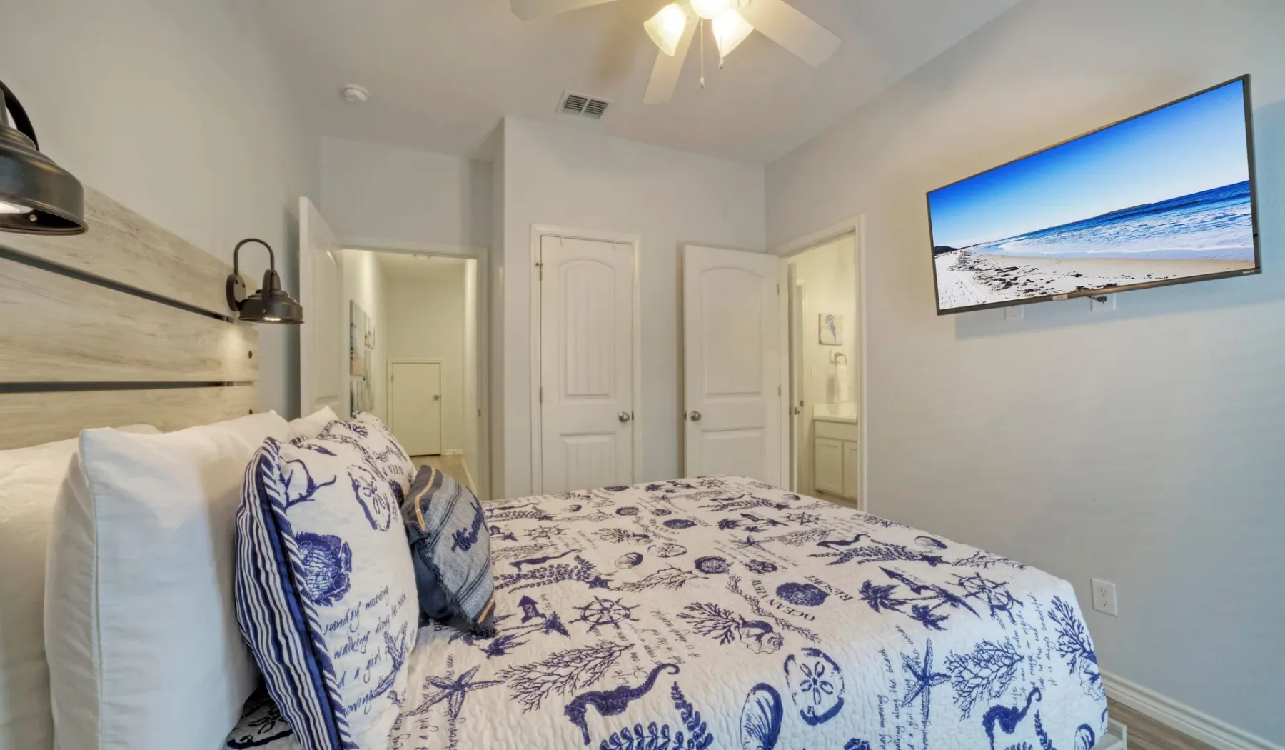 Un dormitorio con una cama cubierta con ropa de cama estampada en azul y blanco y un televisor en la pared.
