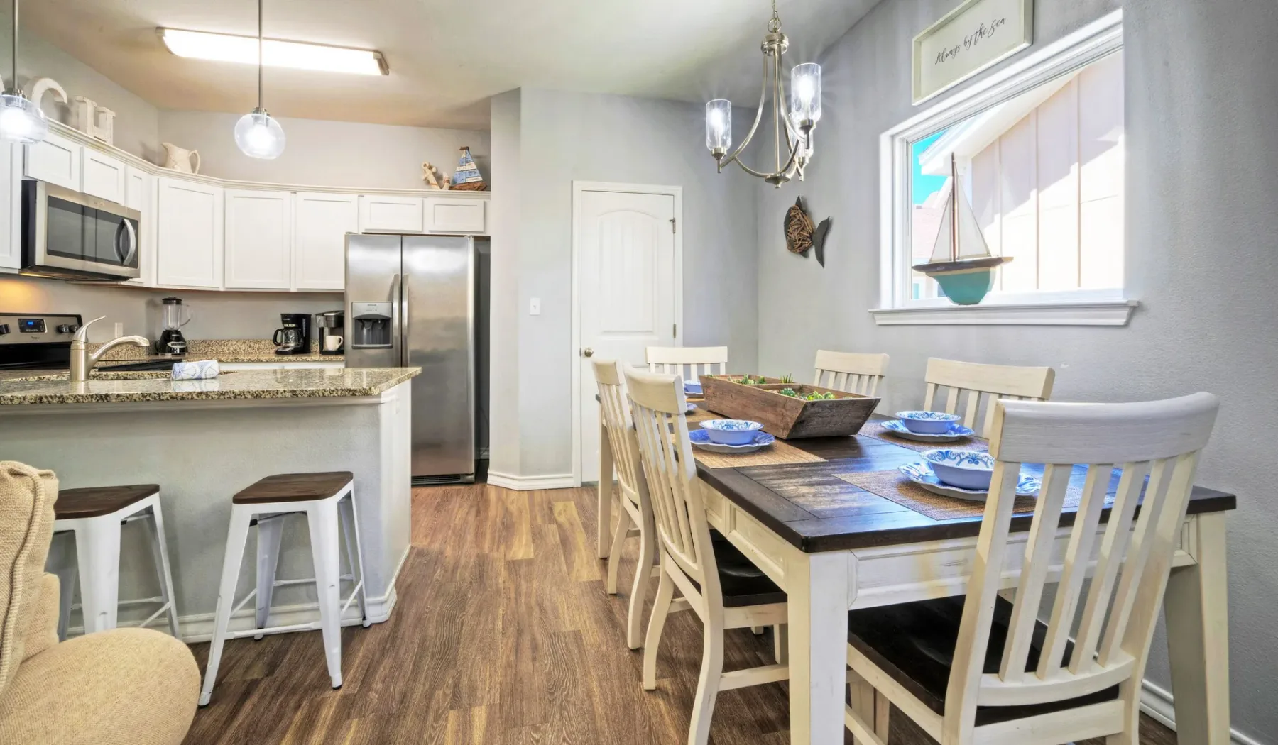 Comedor junto a una cocina abierta, con la mesa puesta y gabinetes blancos.