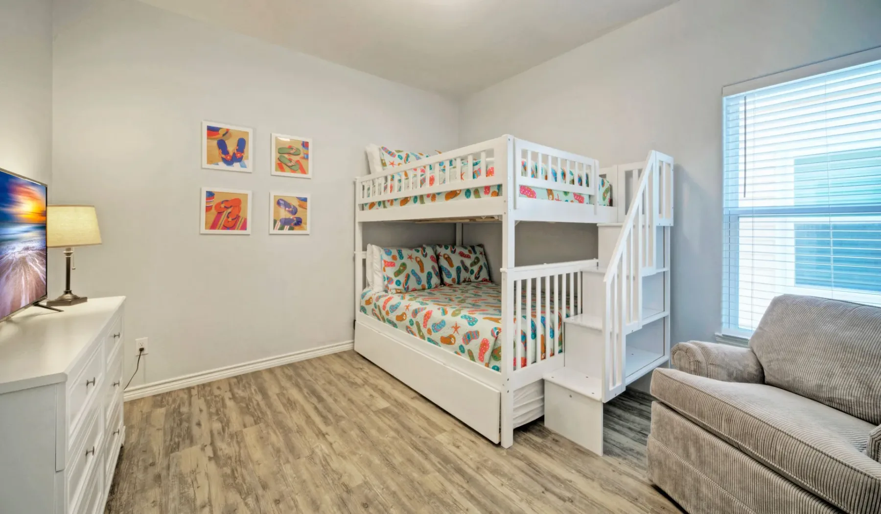 Un dormitorio luminoso cuenta con literas blancas, ropa de cama colorida y una ventana grande.