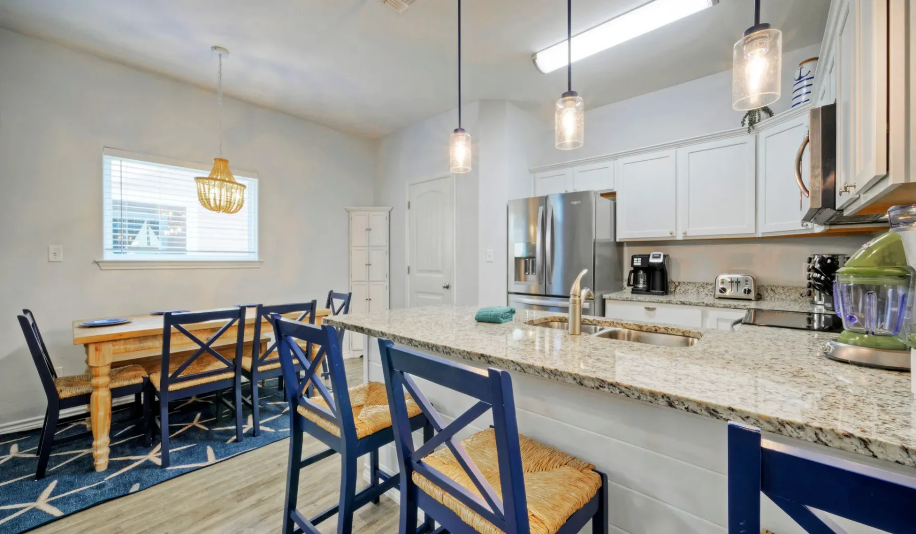 Una cocina y comedor con una isla larga, asientos junto a la barra y una mesa de madera.