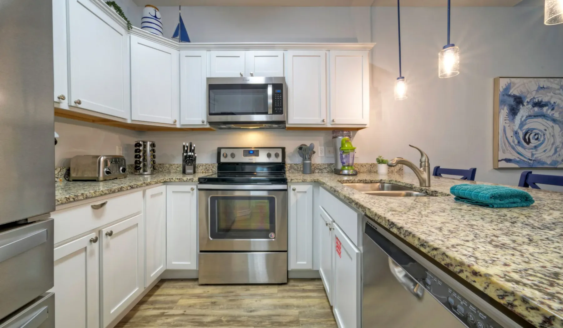 Una cocina luminosa con gabinetes blancos, electrodomésticos de acero inoxidable y una encimera de piedra.