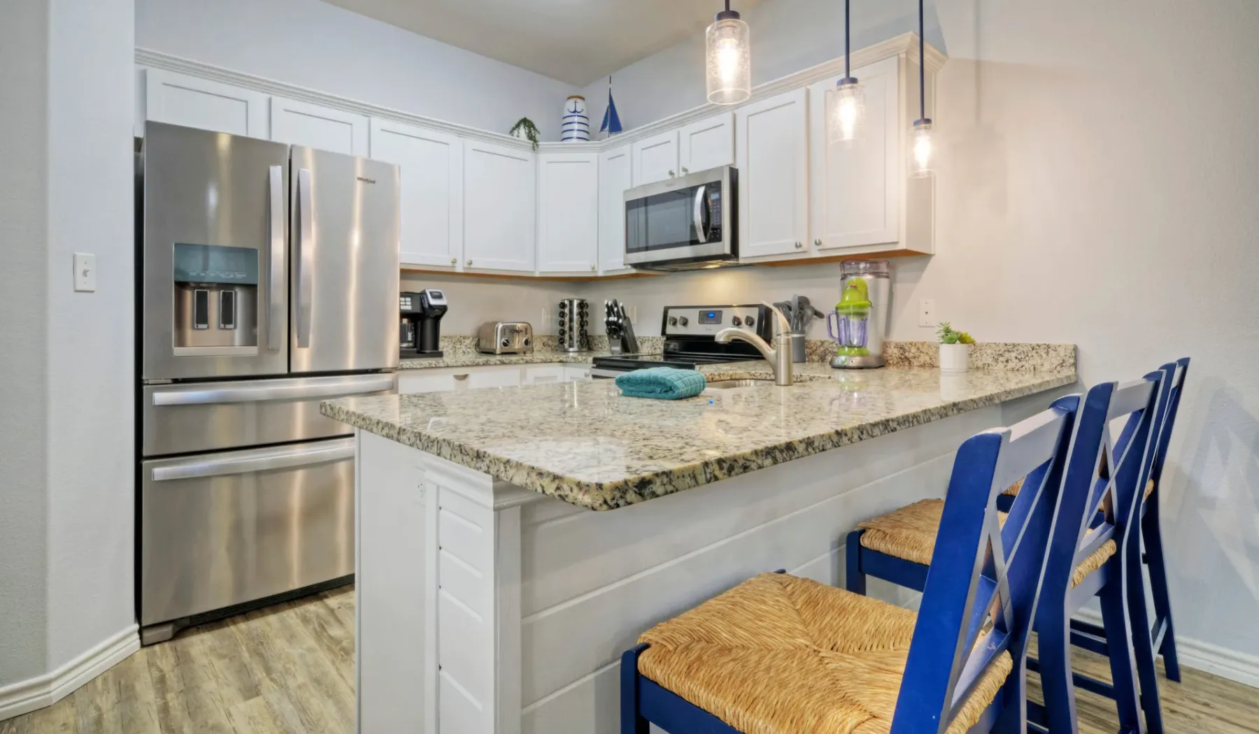 Una cocina luminosa con una isla de piedra y asientos azules.