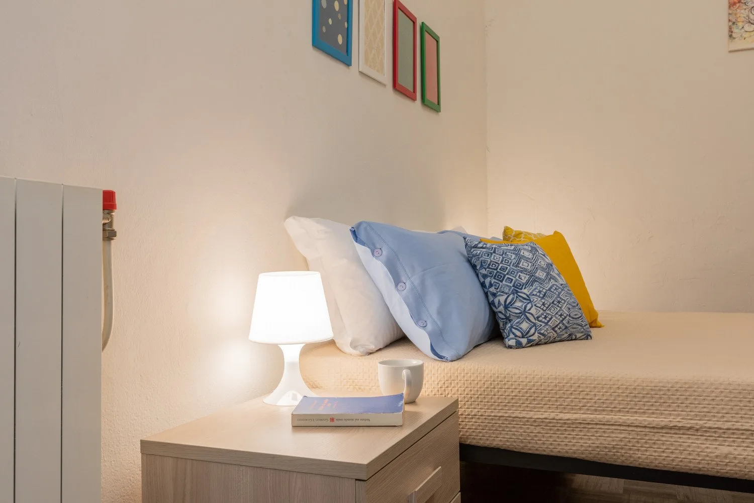 Un dormitorio con una cama, almohadas de colores y una lámpara encendida.