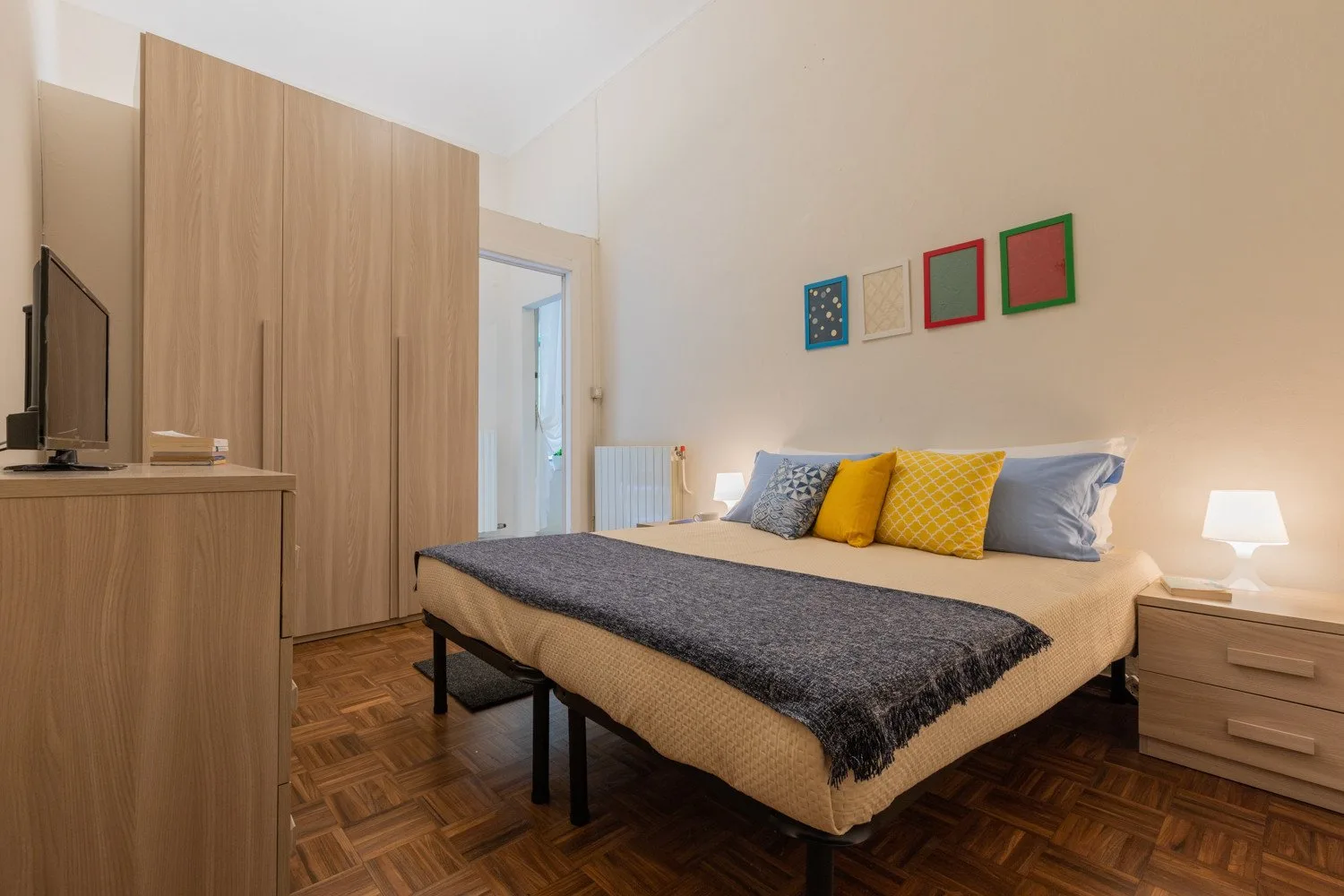 Un dormitorio con una cama tendida, una mesita de noche y suelo de madera.