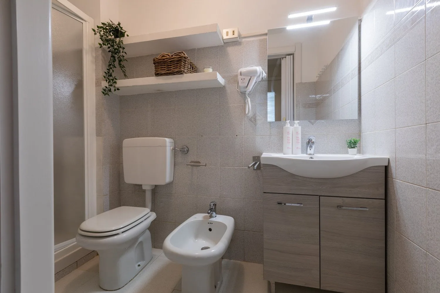 Un baño alicatado con inodoro, bidé y lavabo bajo un espejo.