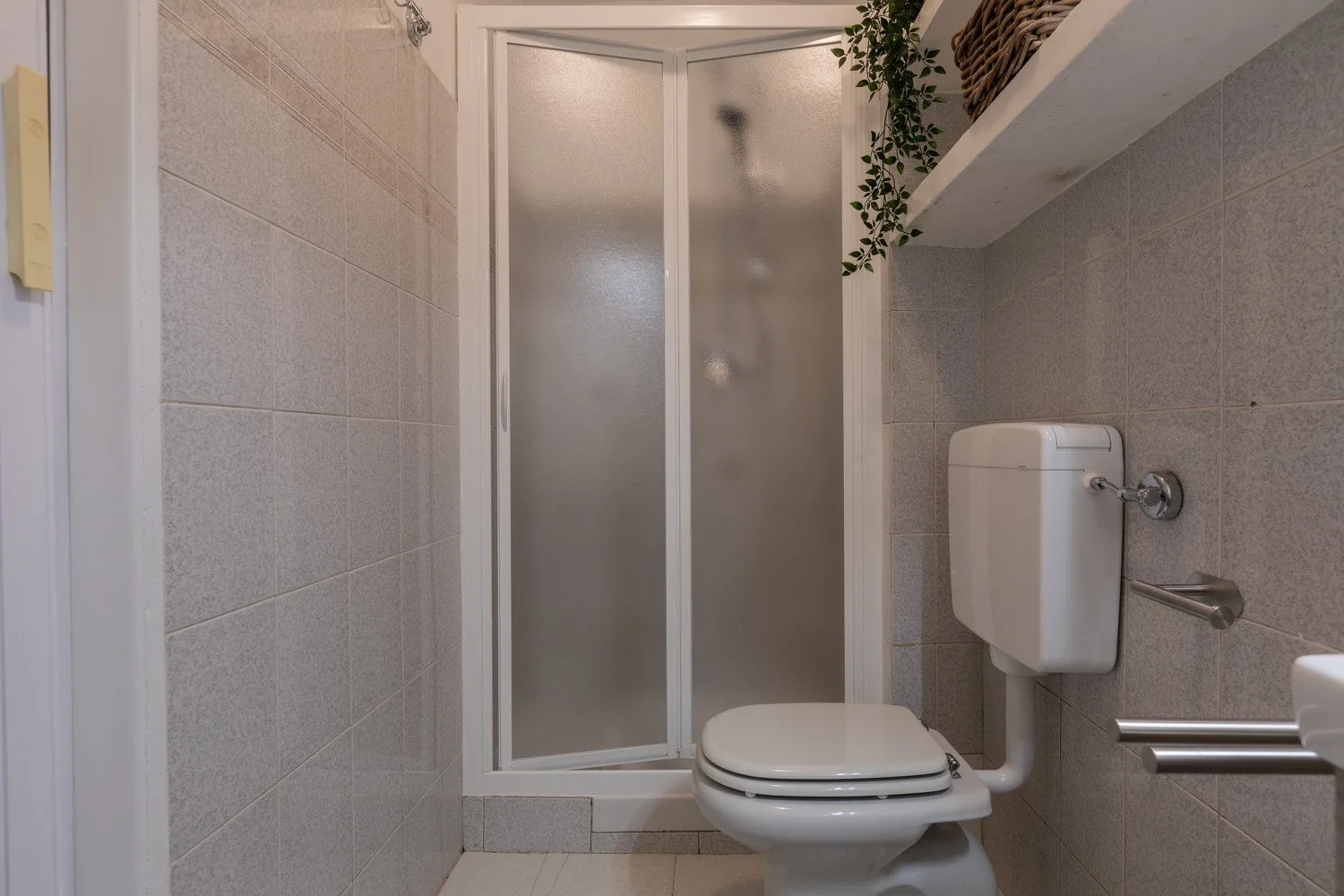 Un baño con azulejos, un inodoro y una ducha con vidrio esmerilado.