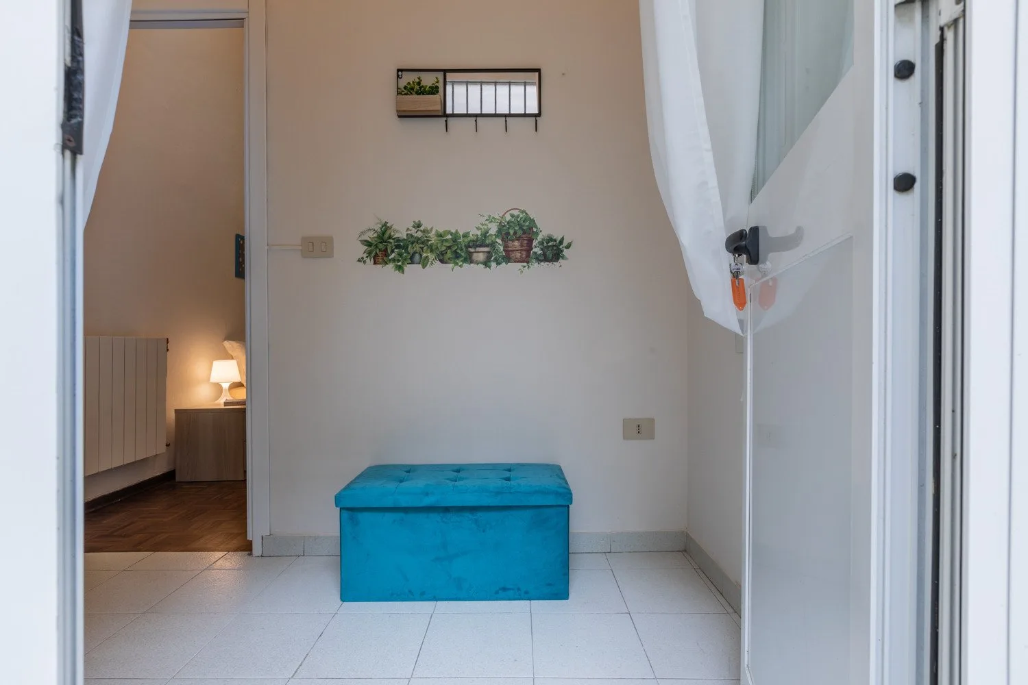 Una pequeña entrada con un banco azul con almacenamiento y plantas en la pared.