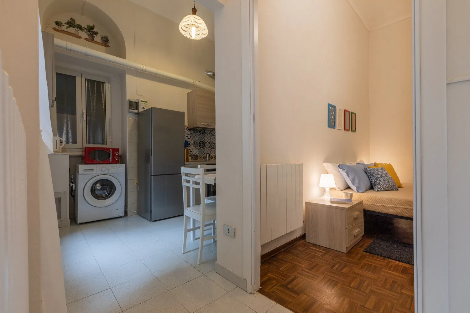 Un dormitorio con cama y mesita de noche da a una cocina compacta.