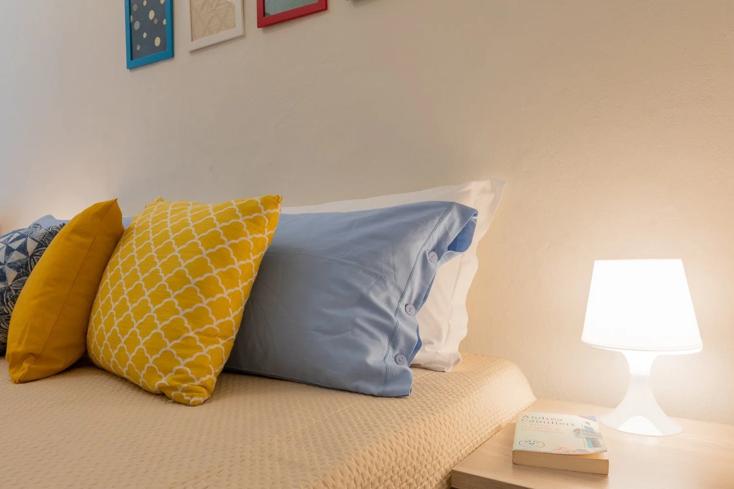 Una cama con almohadas coloridas está junto a una lámpara encendida.