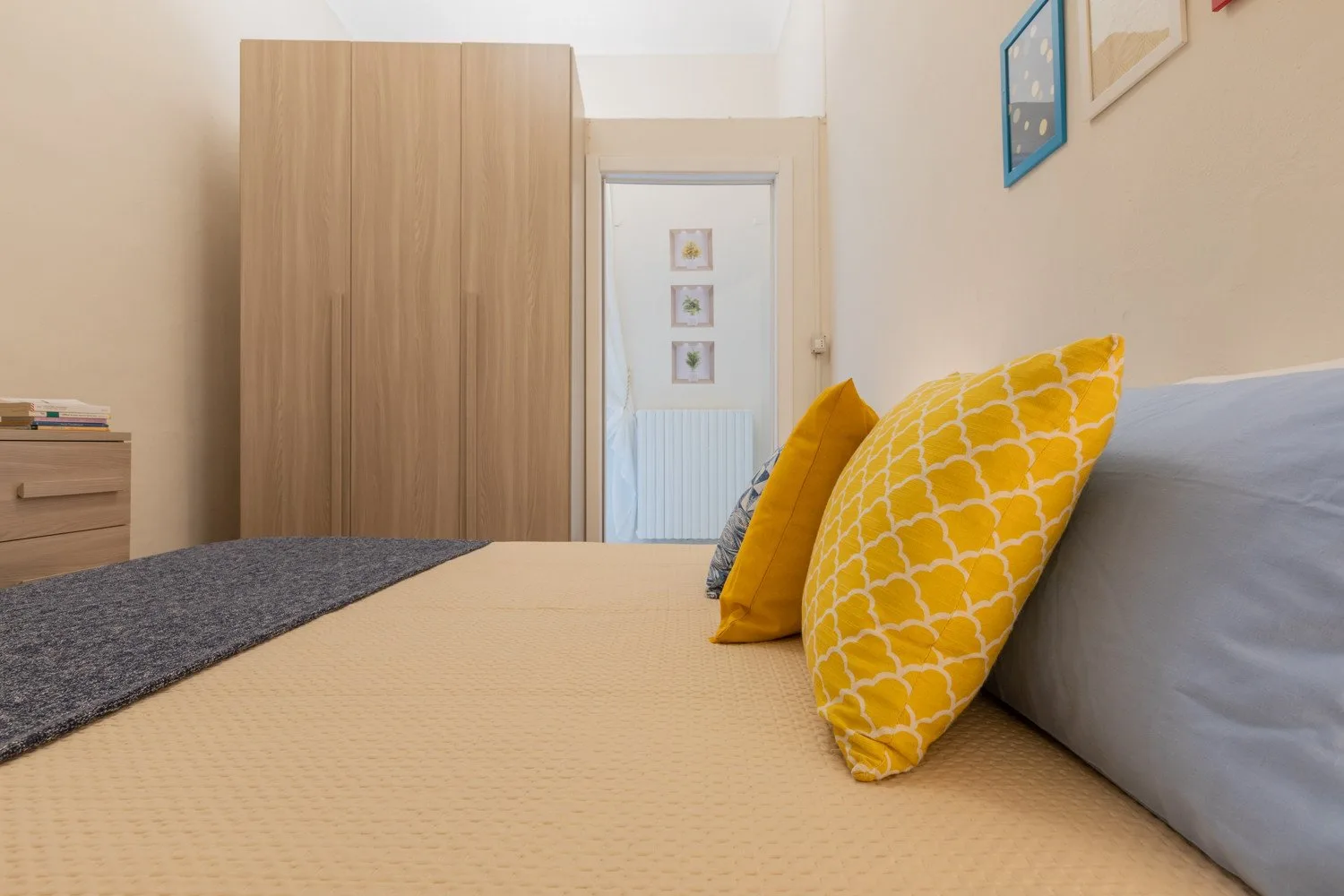 Un dormitorio con una cama, cojines amarillos estampados y un armario de madera.