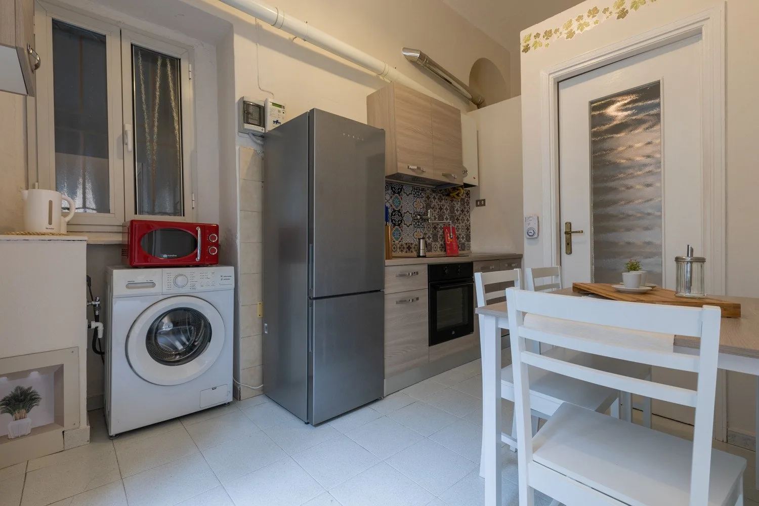 Una cocina compacta con zona de comedor y sillas blancas junto a un refrigerador de acero inoxidable.