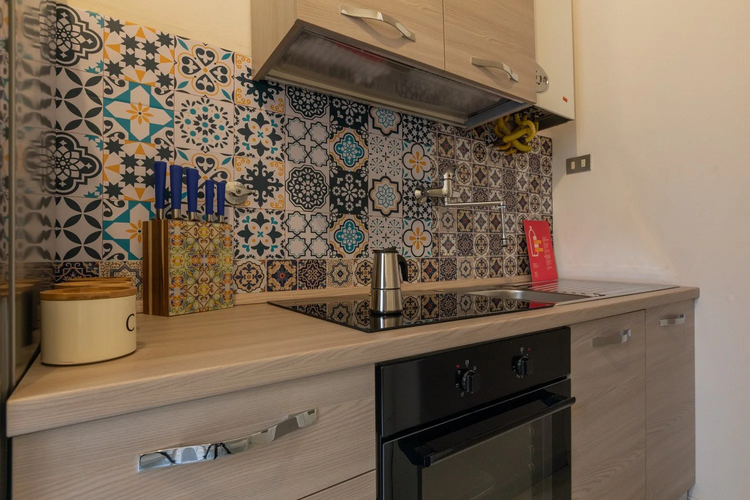 Una cocina compacta con placa de cocción, horno y un colorido salpicadero estampado.