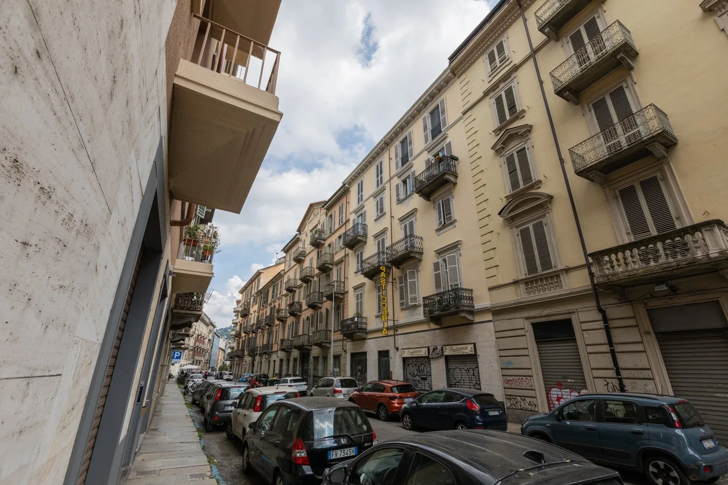 Una calle urbana estrecha flanqueada por edificios de apartamentos y coches aparcados.