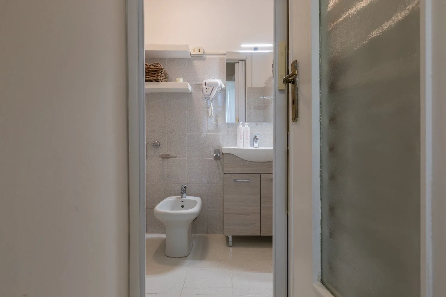 Un baño con lavabo, inodoro y mueble de lavabo visible a través de una puerta abierta.
