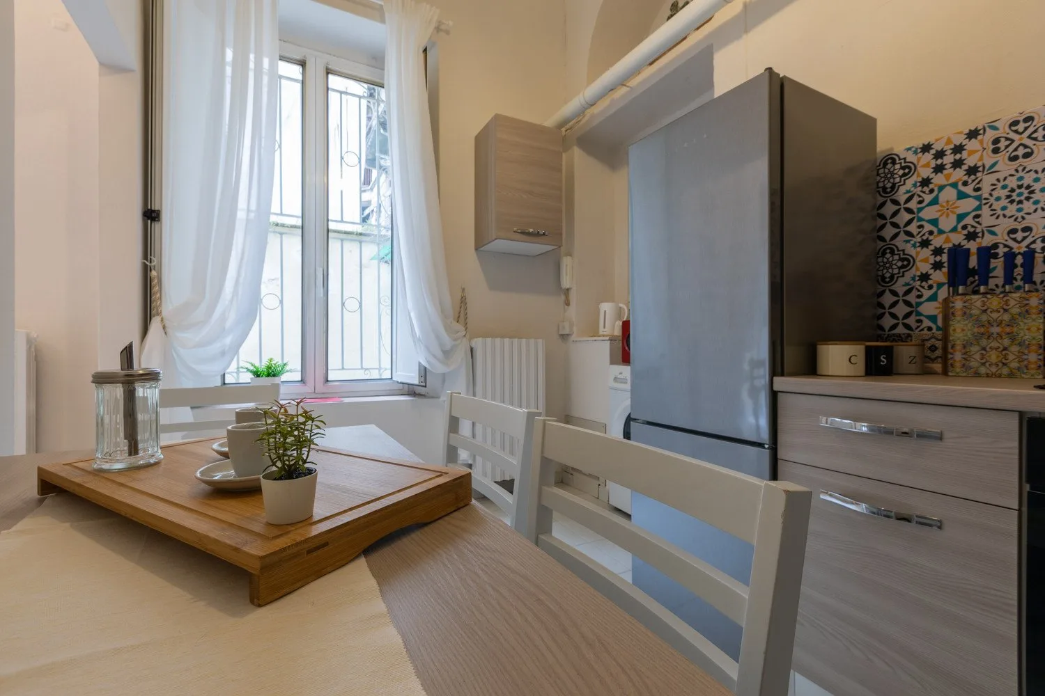 Una zona de comedor en la cocina con una mesa de madera, sillas blancas y un refrigerador.
