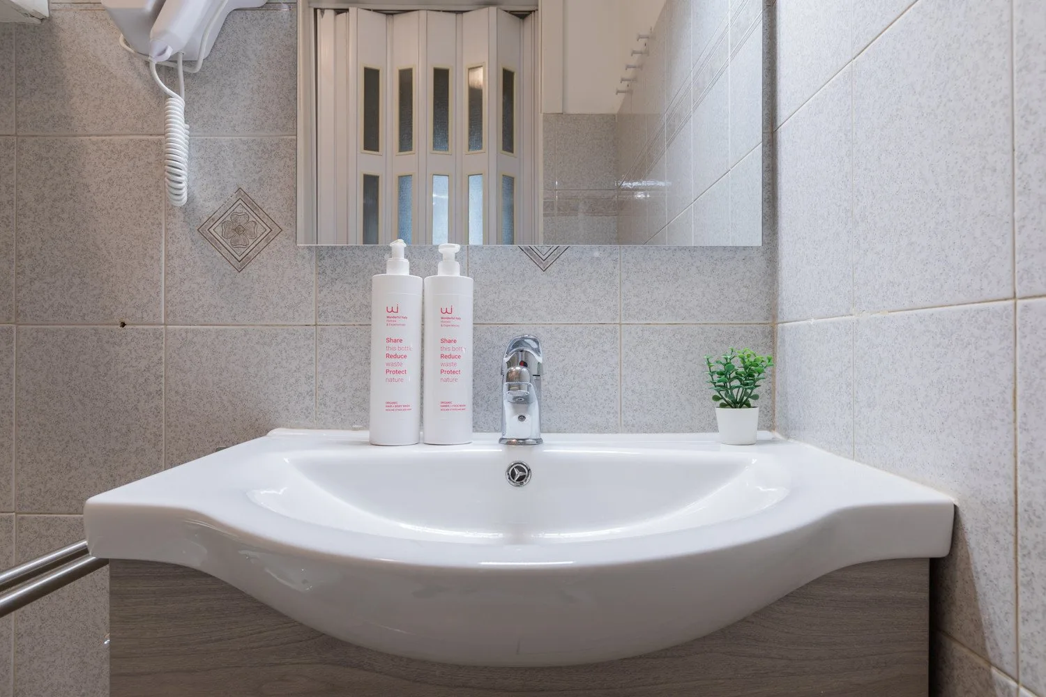 Un lavabo de baño está bajo un armario con espejo, con artículos de aseo y una pequeña planta cerca.