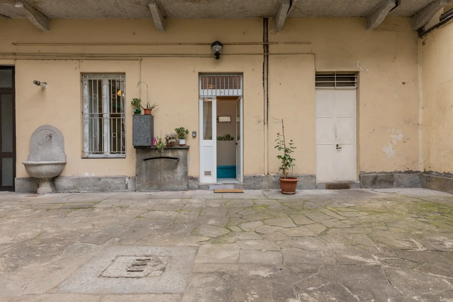 Un patio pavimentado con una fachada clara, puertas, ventanas y plantas en macetas.