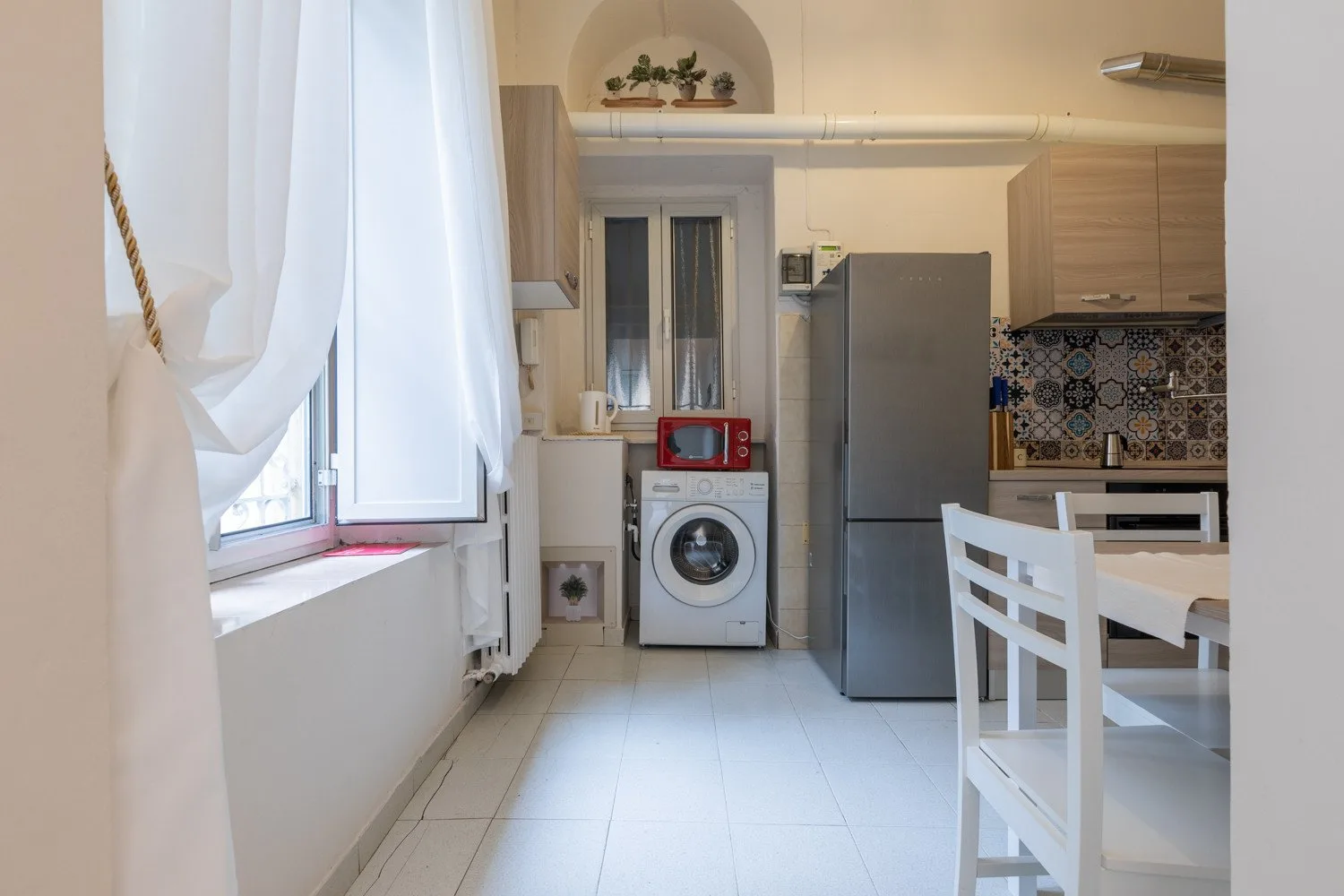 Una cocina luminosa con refrigerador, lavadora y mesa de comedor.
