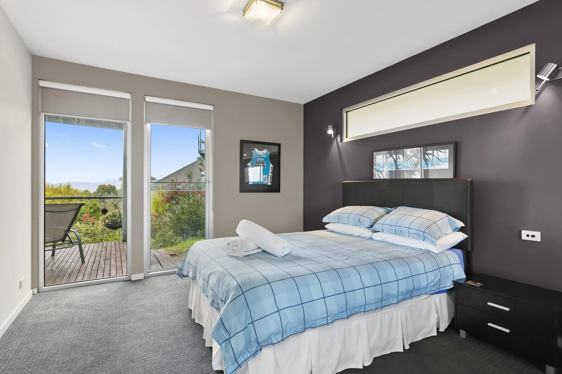 A bedroom with a bed beside tall windows overlooking greenery.
