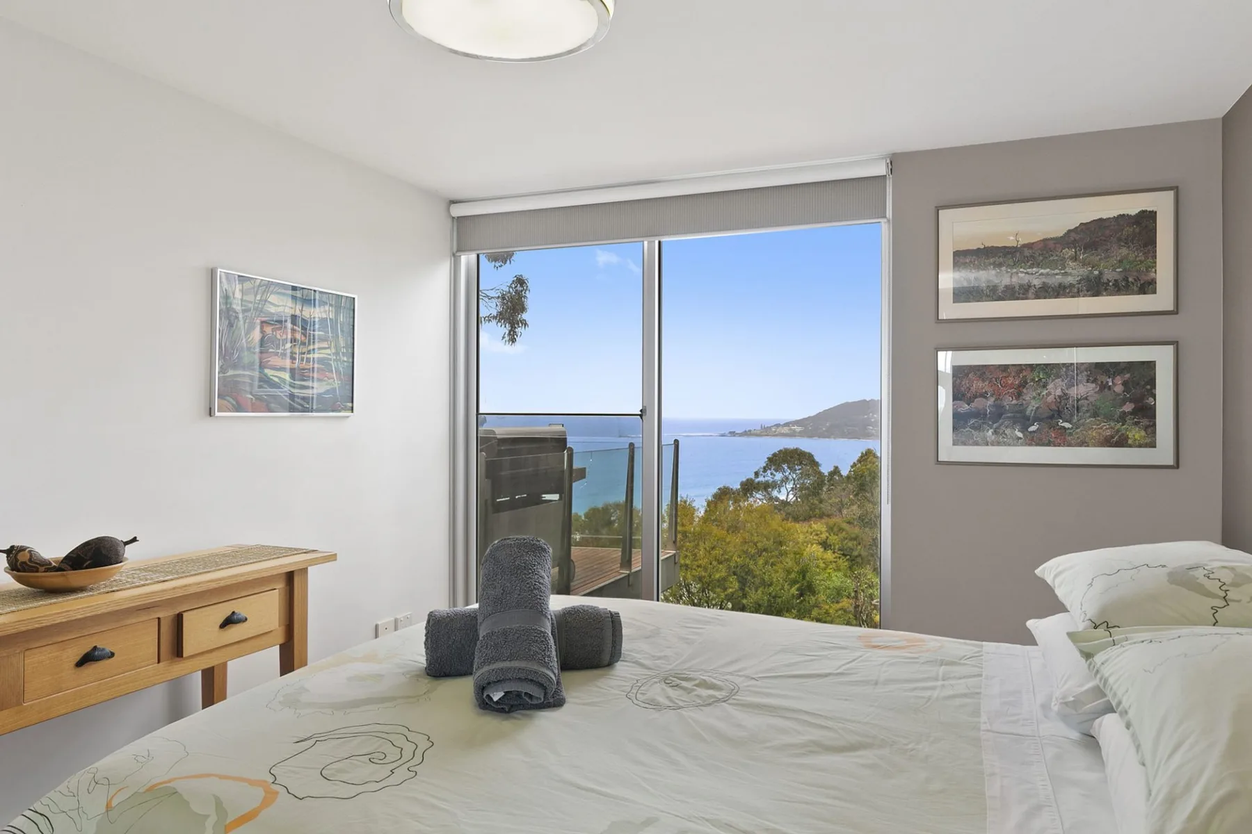 A bedroom with a large window overlooking the ocean and nearby trees.