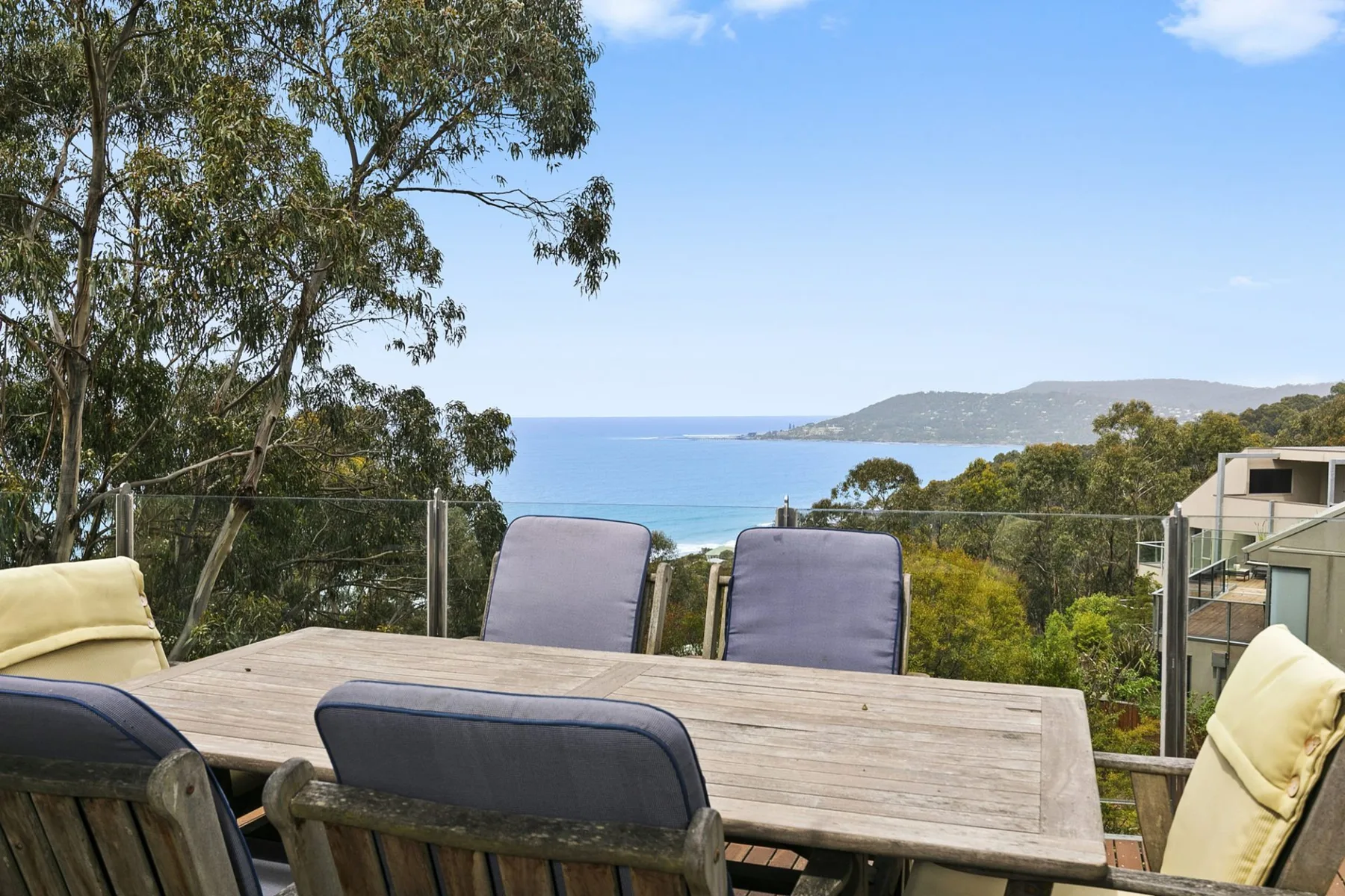 An outdoor dining area overlooks a coastal bay and distant headland.