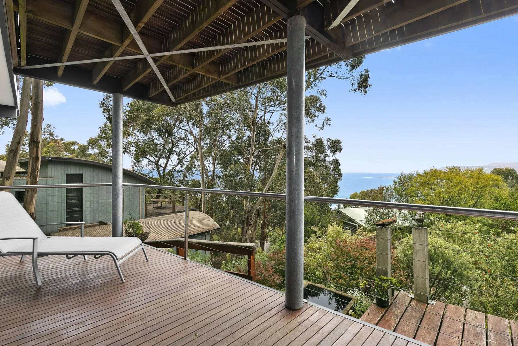 A covered outdoor deck with seating overlooks trees and a distant stretch of water.