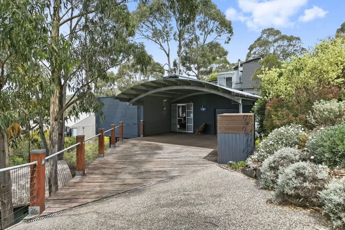 A timber walkway leads to a dark building beside landscaped greenery.