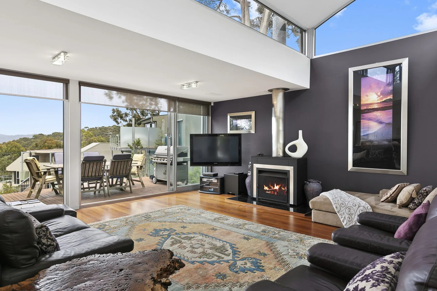 A bright living room opens onto a deck through wide glass doors.