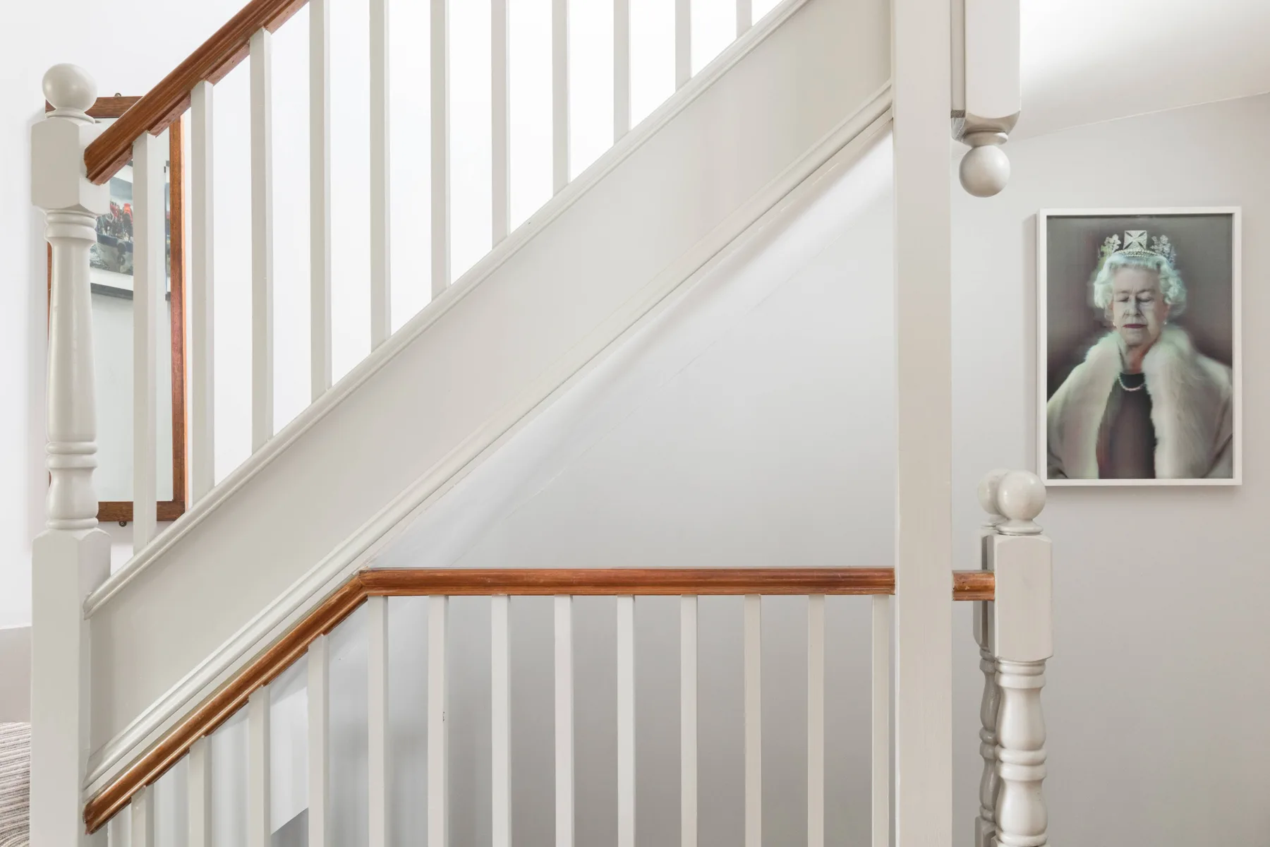 Una escalera blanca con pasamanos de madera está junto a un retrato enmarcado.