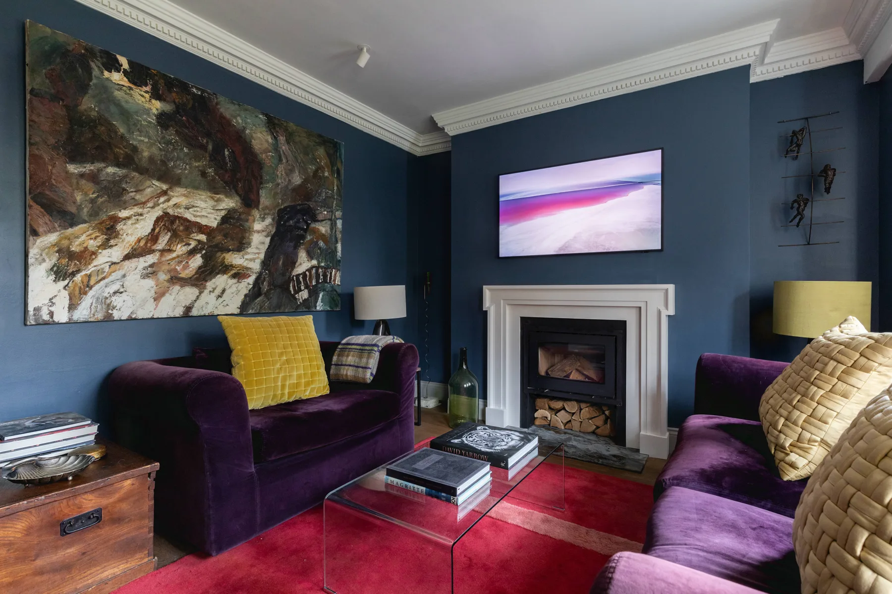 Una sala azul con asientos morados, una chimenea y obras de arte coloridas.
