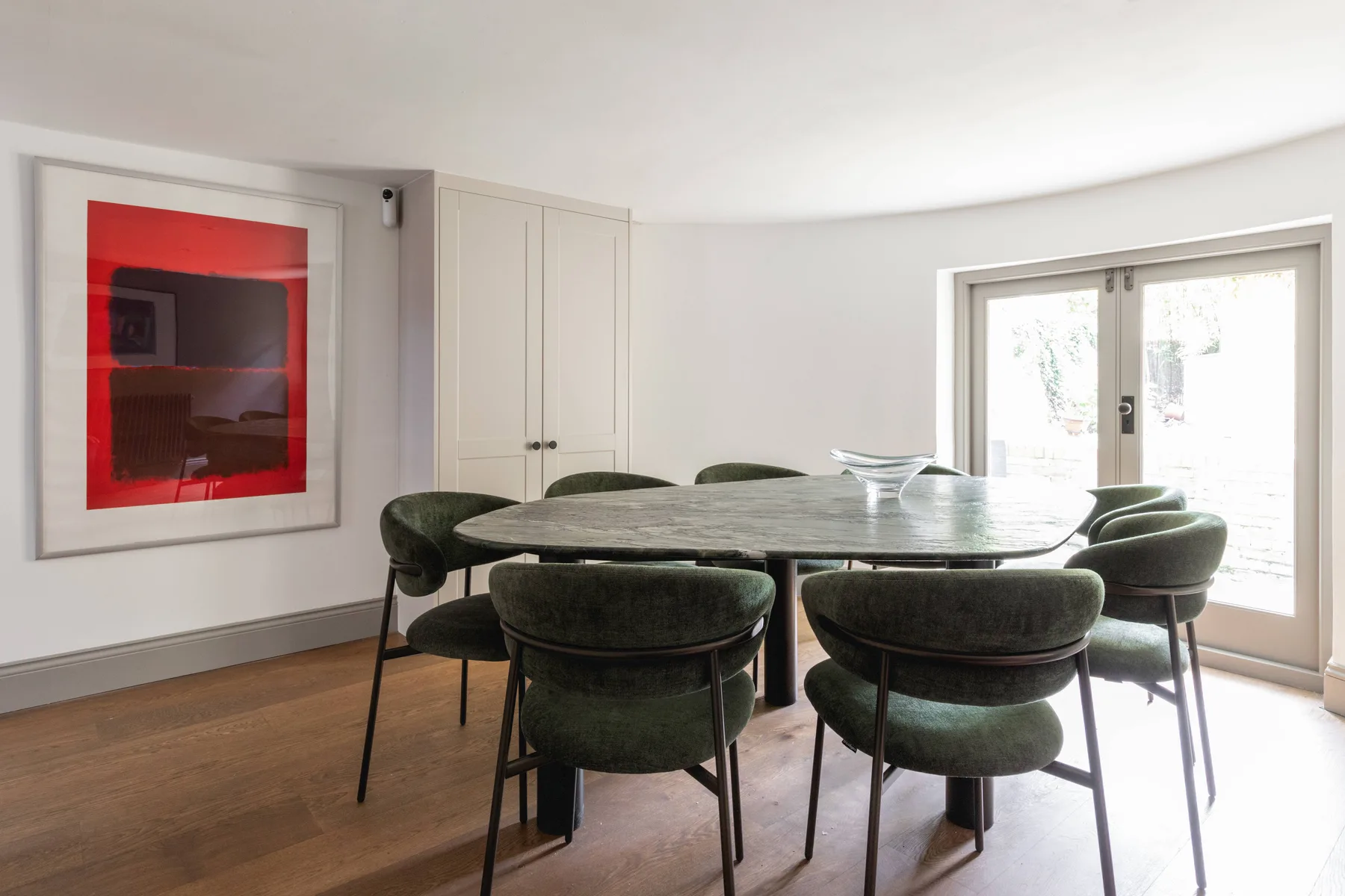 Comedor con una mesa grande y asientos tapizados de color verde junto a ventanas luminosas.