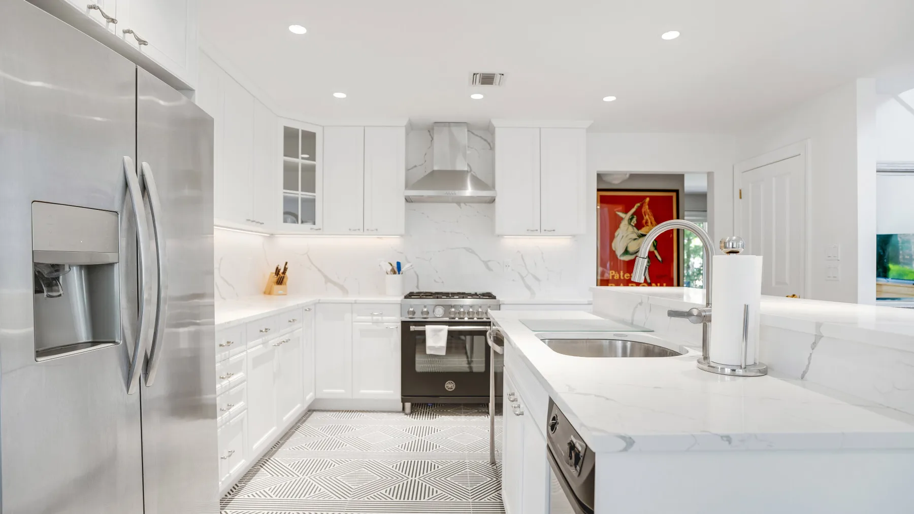 Una cocina luminosa con gabinetes blancos, electrodomésticos de acero inoxidable e isla central.