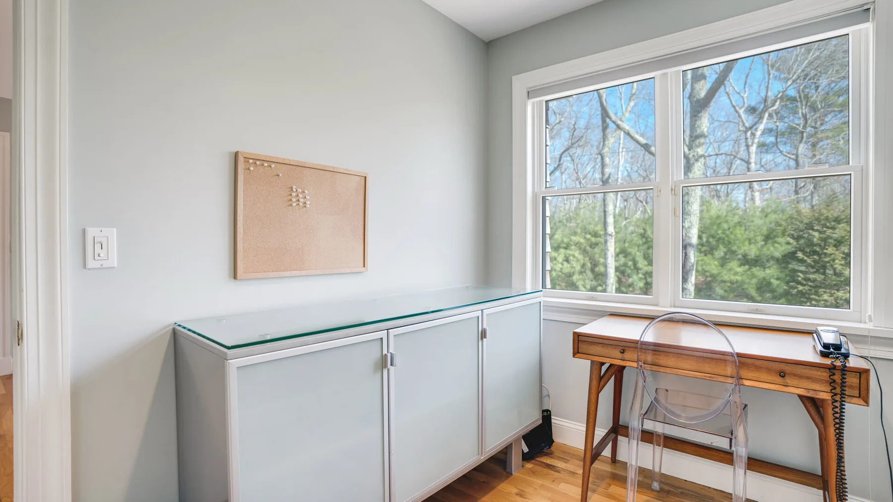 Una habitación luminosa con un mueble largo, un escritorio de madera y ventanas grandes.