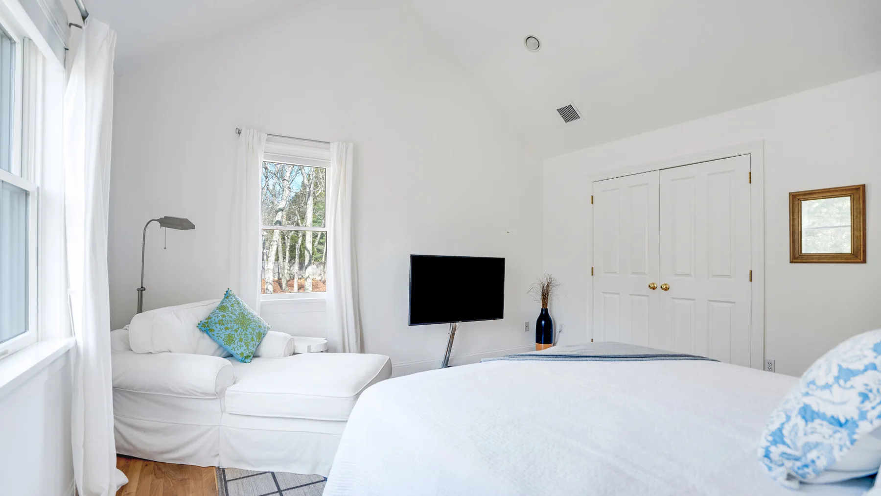 Un dormitorio luminoso con una cama, asientos blancos y ventanas.