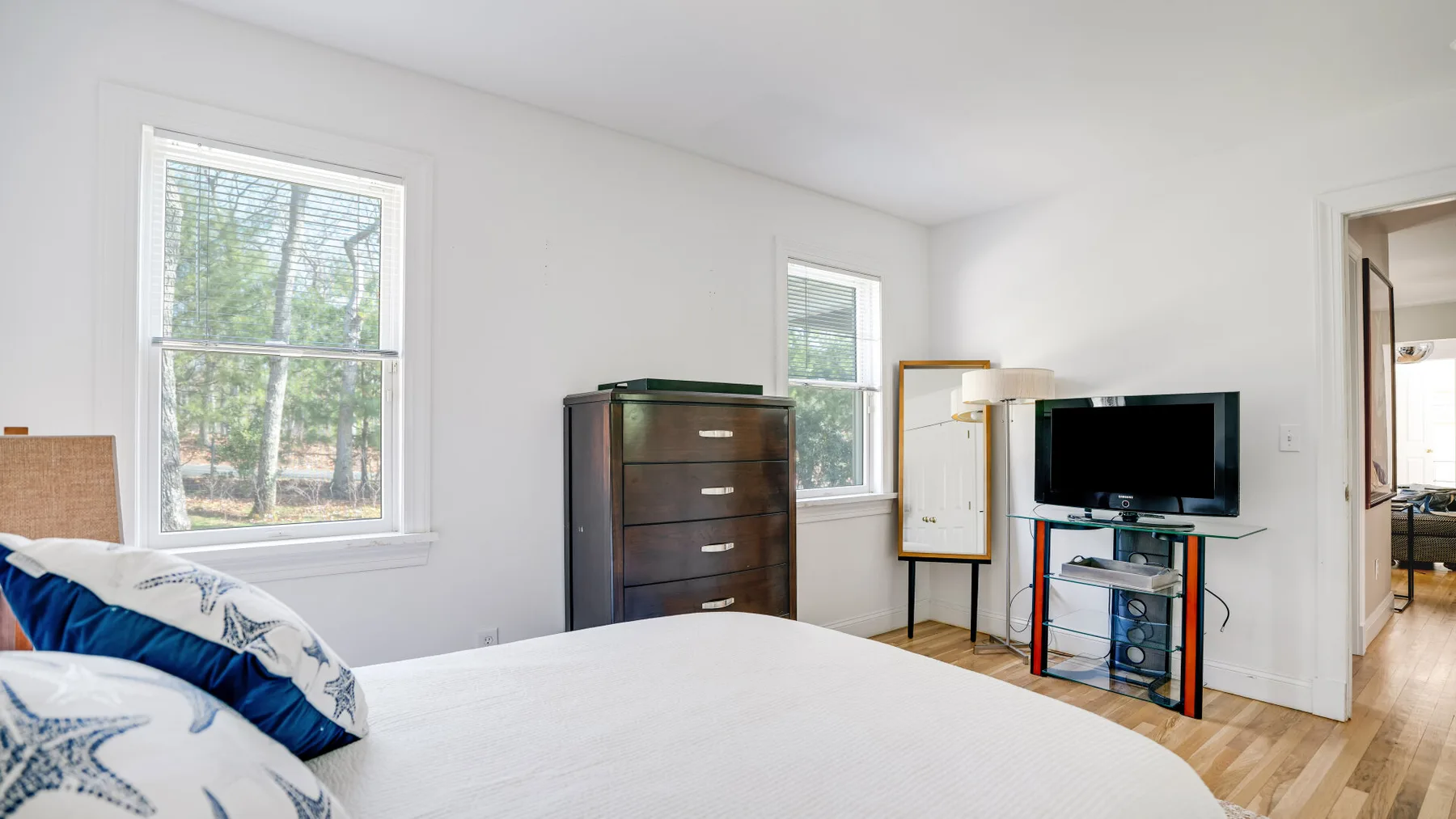 Un dormitorio luminoso con una cama tendida, una cómoda y un televisor.