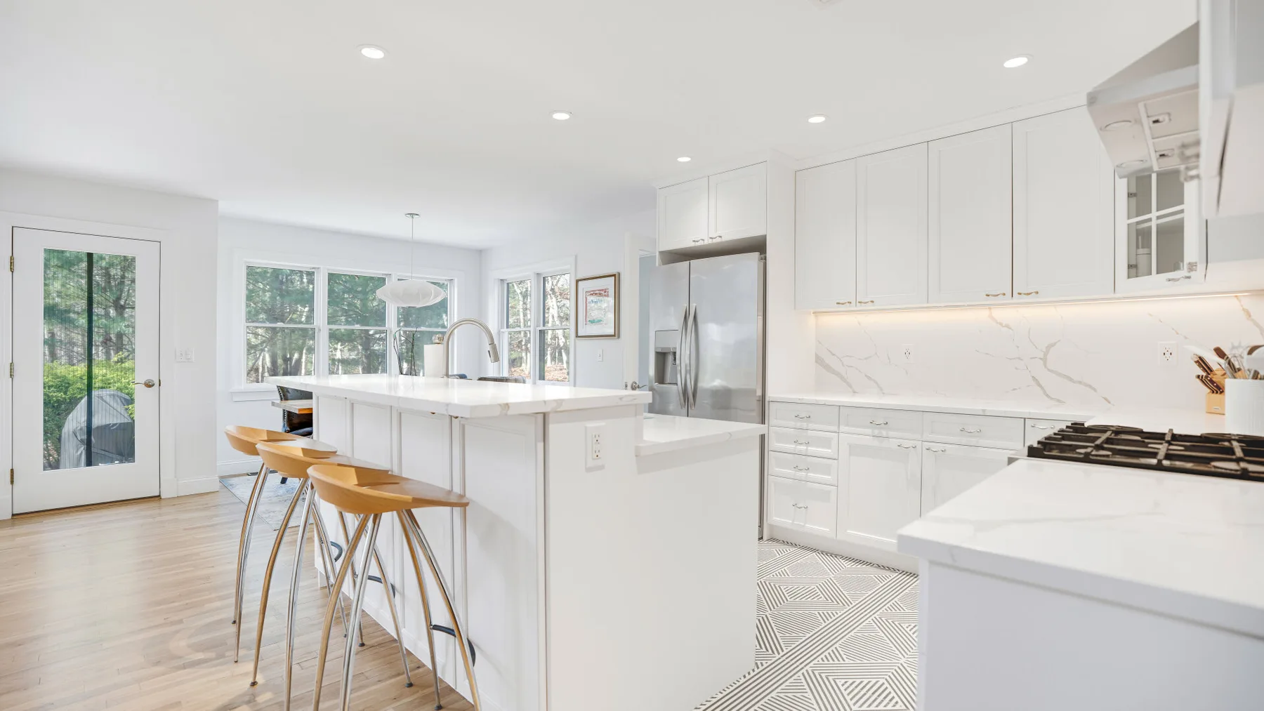 Una cocina luminosa tiene gabinetes blancos, una isla grande y piso de madera clara.