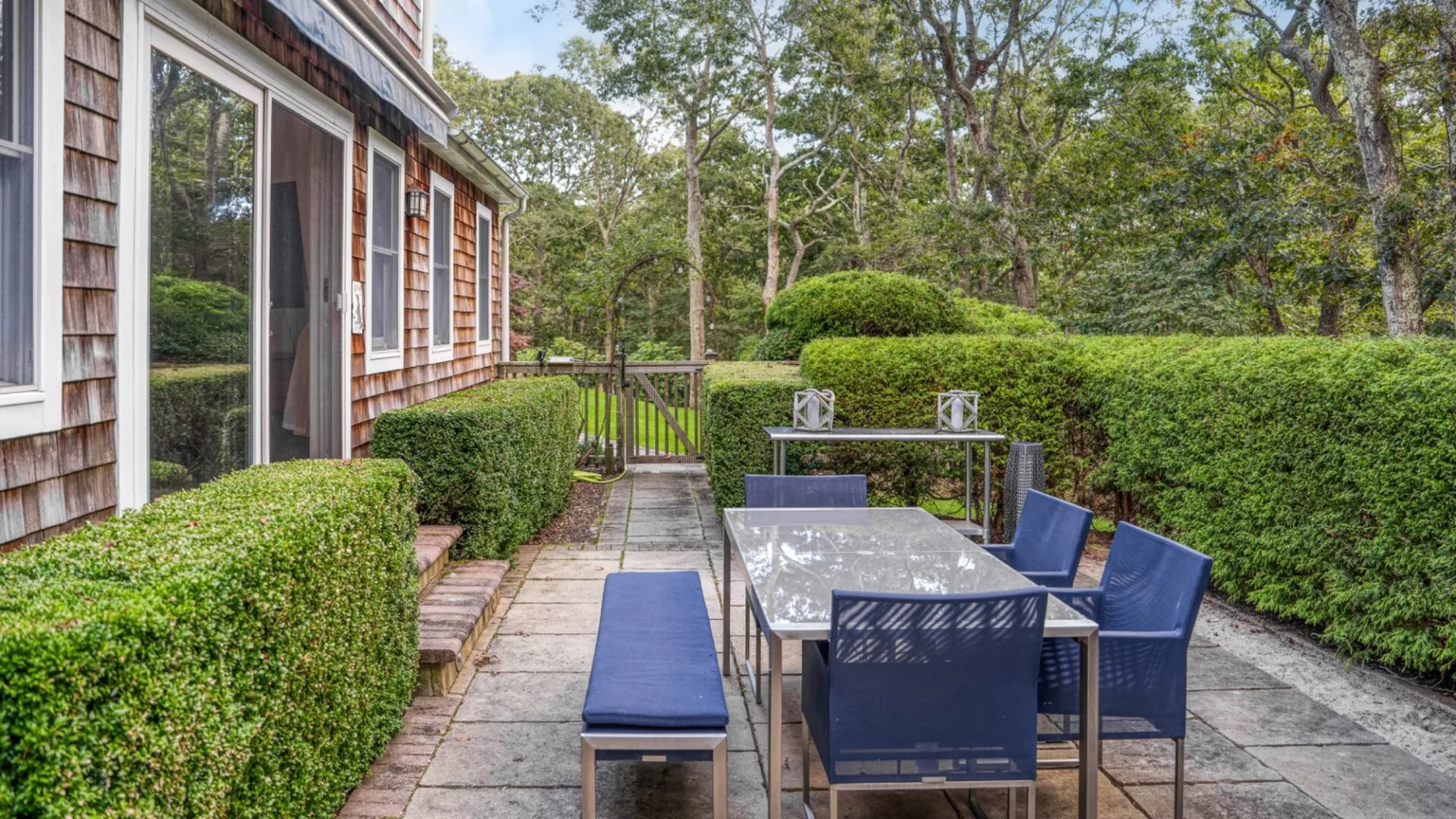 Un patio exterior con mesa de comedor y asientos azules junto a una casa.